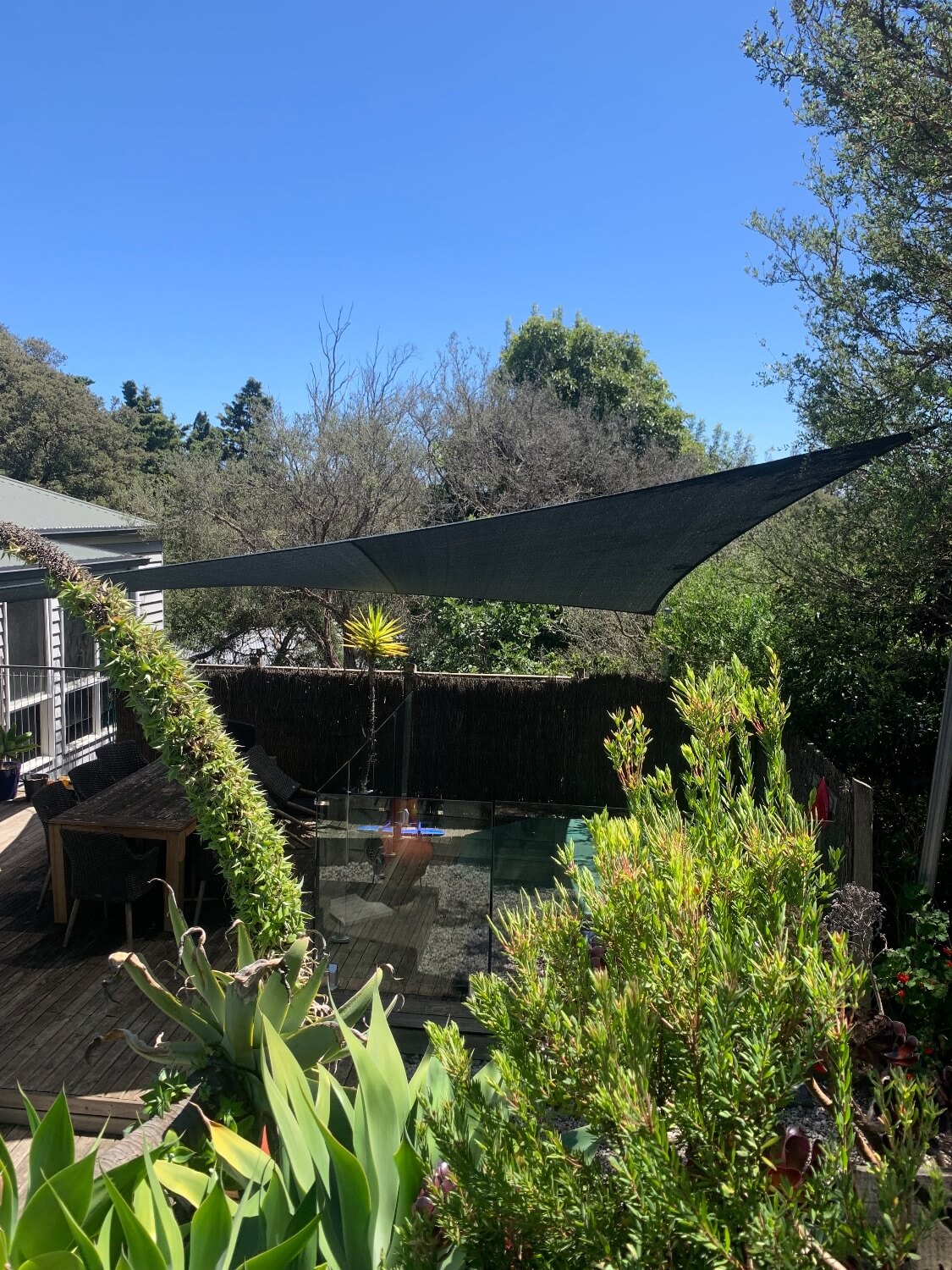 Grey shade sail over decking. Shade cover for table and spa area. native garden shade